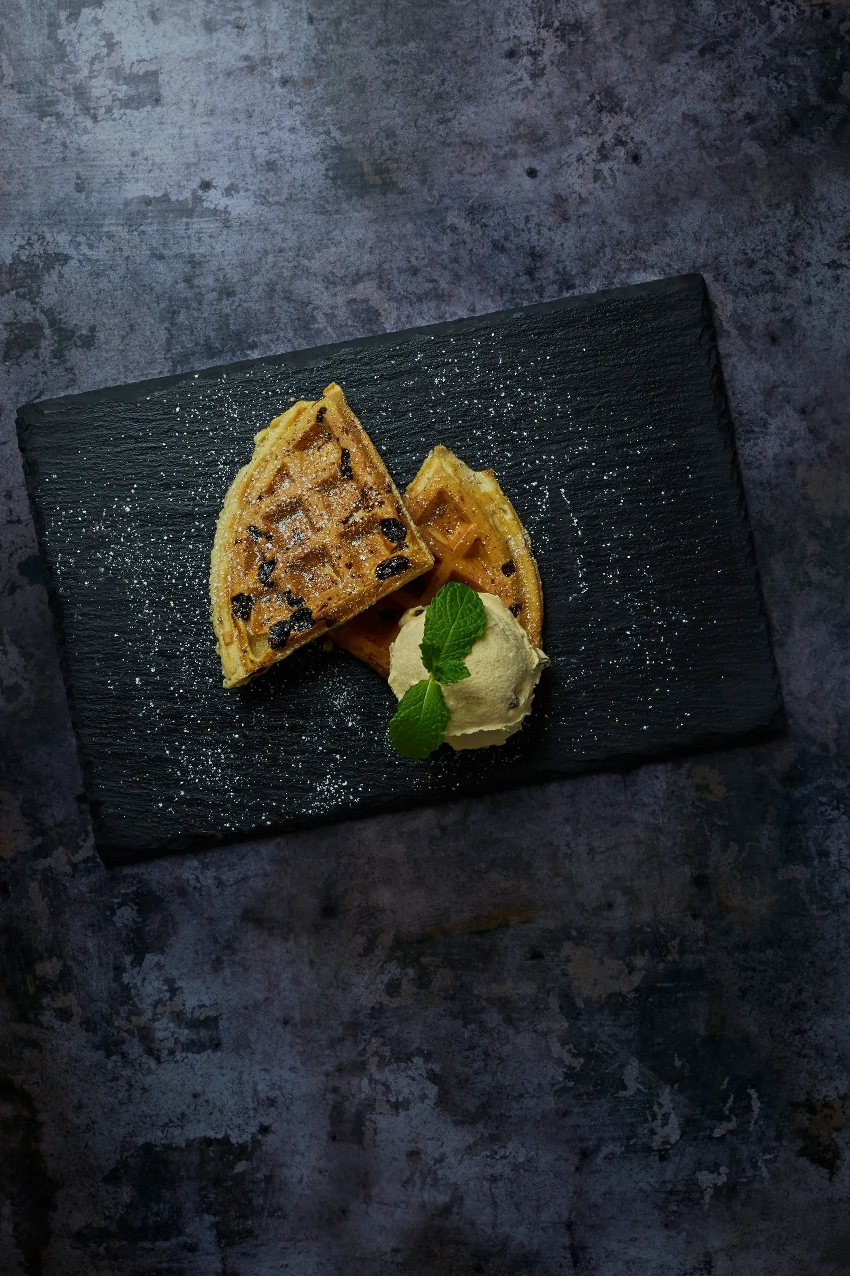 A plated portion of The Welsh Cake Waffle with ice cream and mint on a dark textured background
